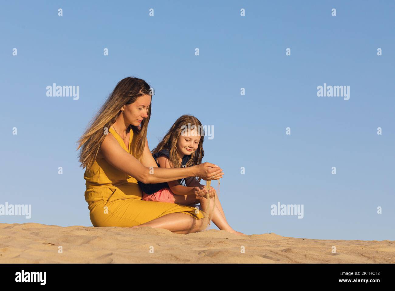 Mom and daughter play with sand on a sunny summer evening Stock Photo