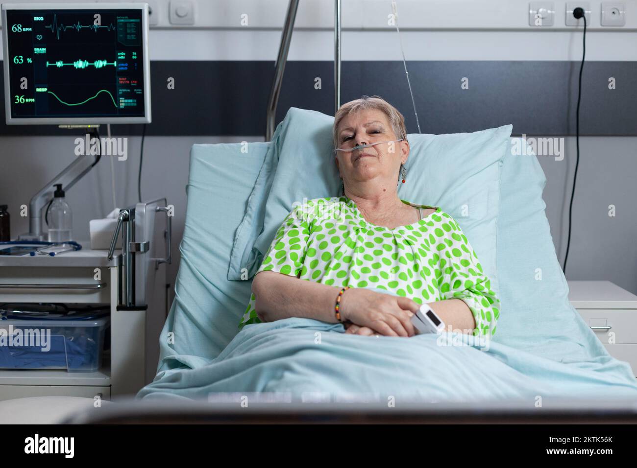 Female patient resting after surgery in hospital monitoring room. Elderly lady connected to medical equipment measuring vital signs. Old woman relaxing in sanatorium recovery bedroom. Stock Photo