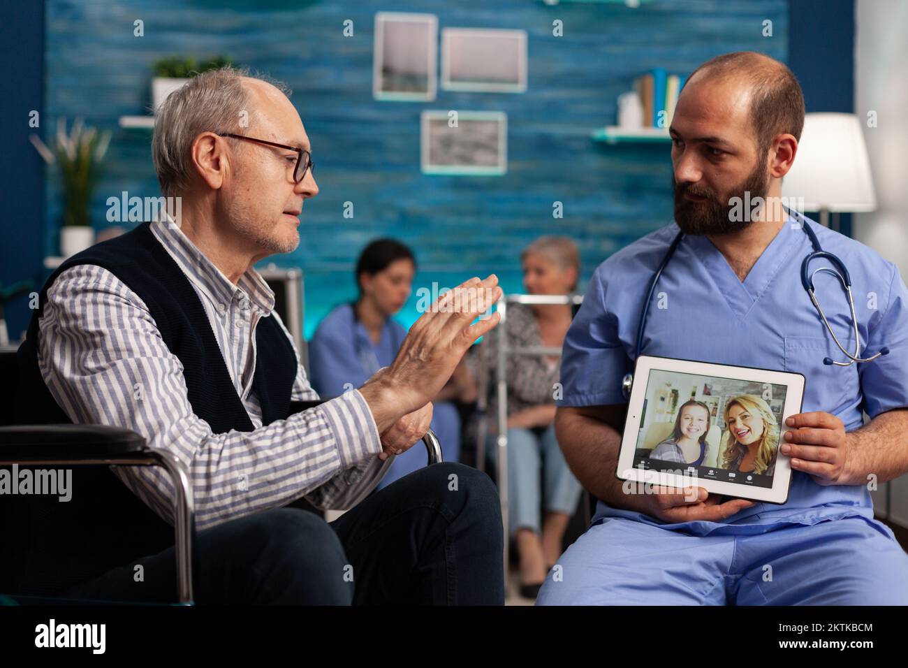 Male nurse helping elderly patient to have a video call with his family using digital tablet. Excited happy senior male talking remotely with his loved ones in nursing home. Stock Photo