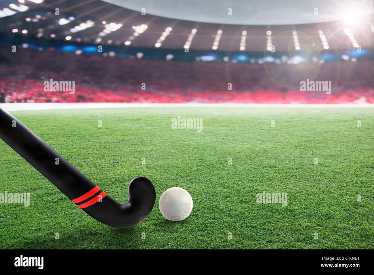 Field hockey stick and ball on grass in brightly lit outdoor stadium with focus on foreground