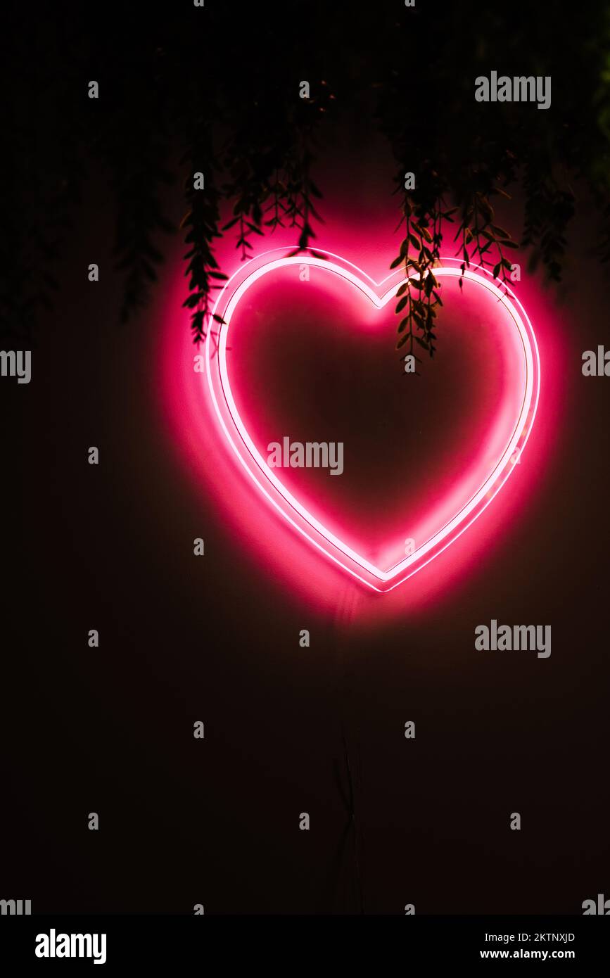 Neon red heart on black wall with copy space Stock Photo
