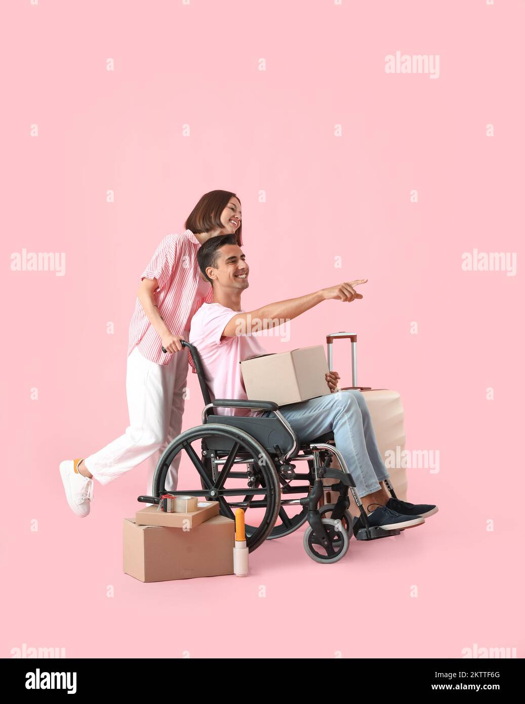 Young woman with her husband in wheelchair and moving boxes on pink