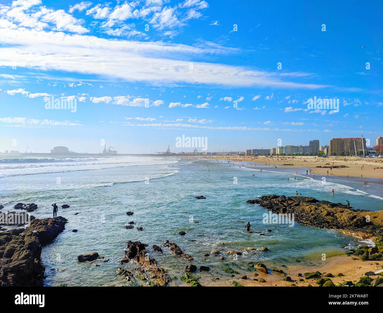 People relaxing at Matosinhos sea beach in sunny day, cityscape with modern architecture and Leixoes port in background, Porto, Portugal Stock Photo