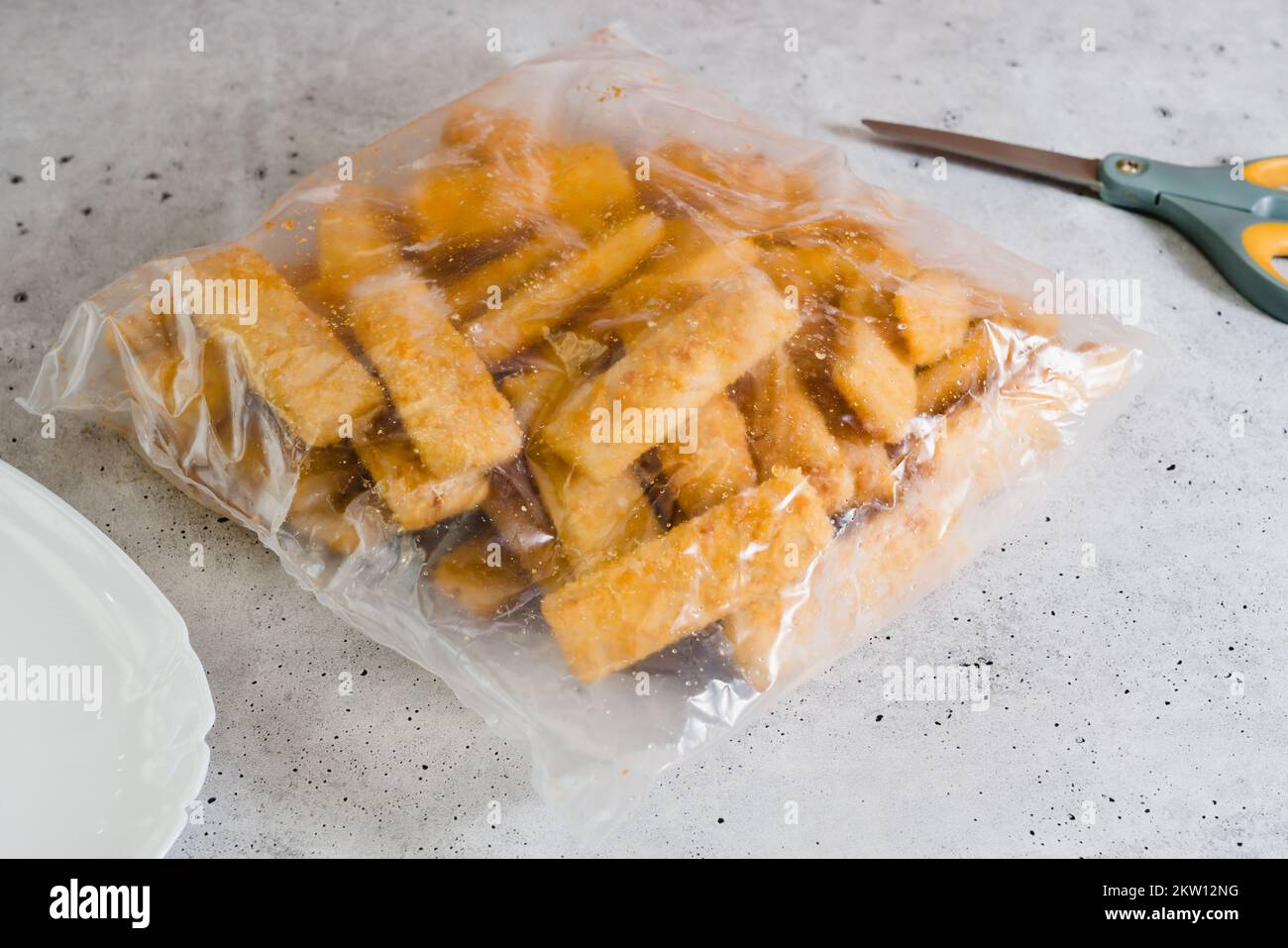 Breaded fish sticks frozen. Plastic bag of fish sticks in a crunchy golden breading close-up on the kitchen table Stock Photo