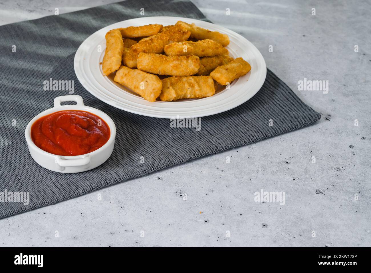 Fish sticks in a crunchy golden breading and bowl of ketchup closeupon