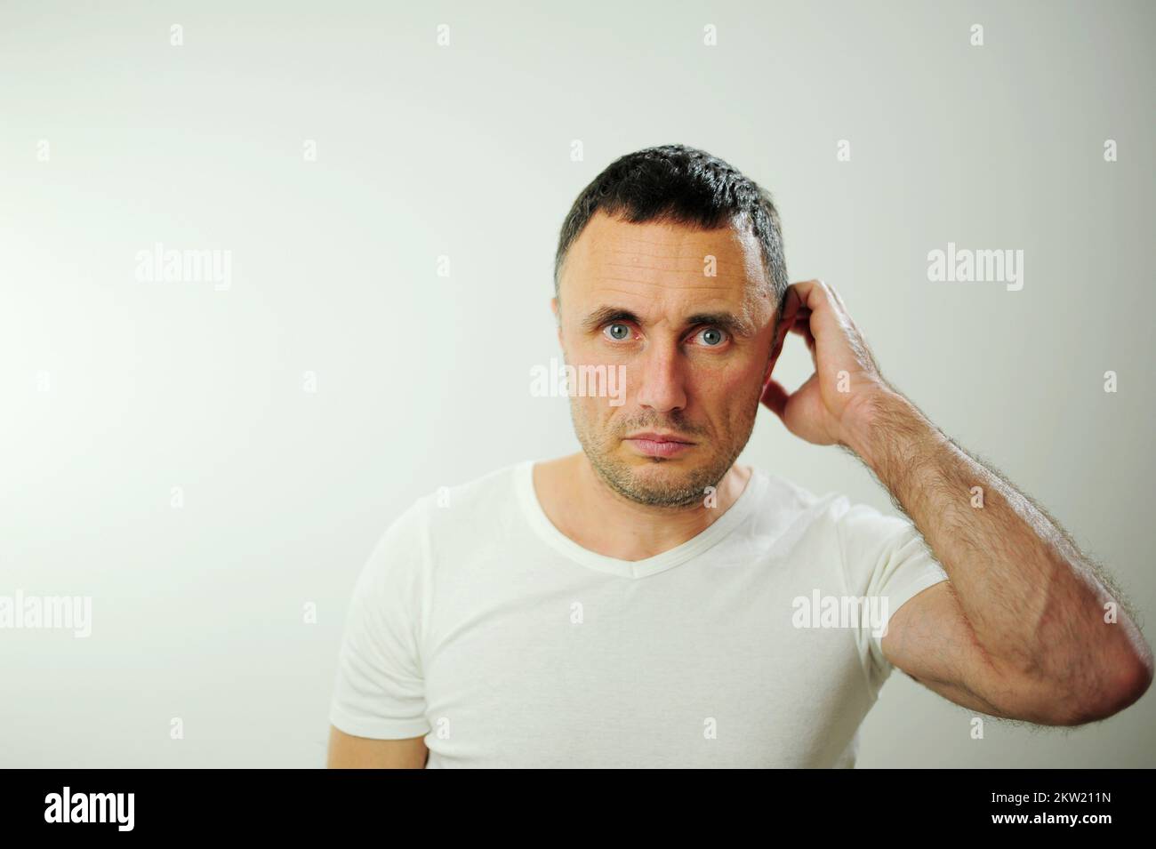 Pensive adult unshaven man scratching back of head and looking away