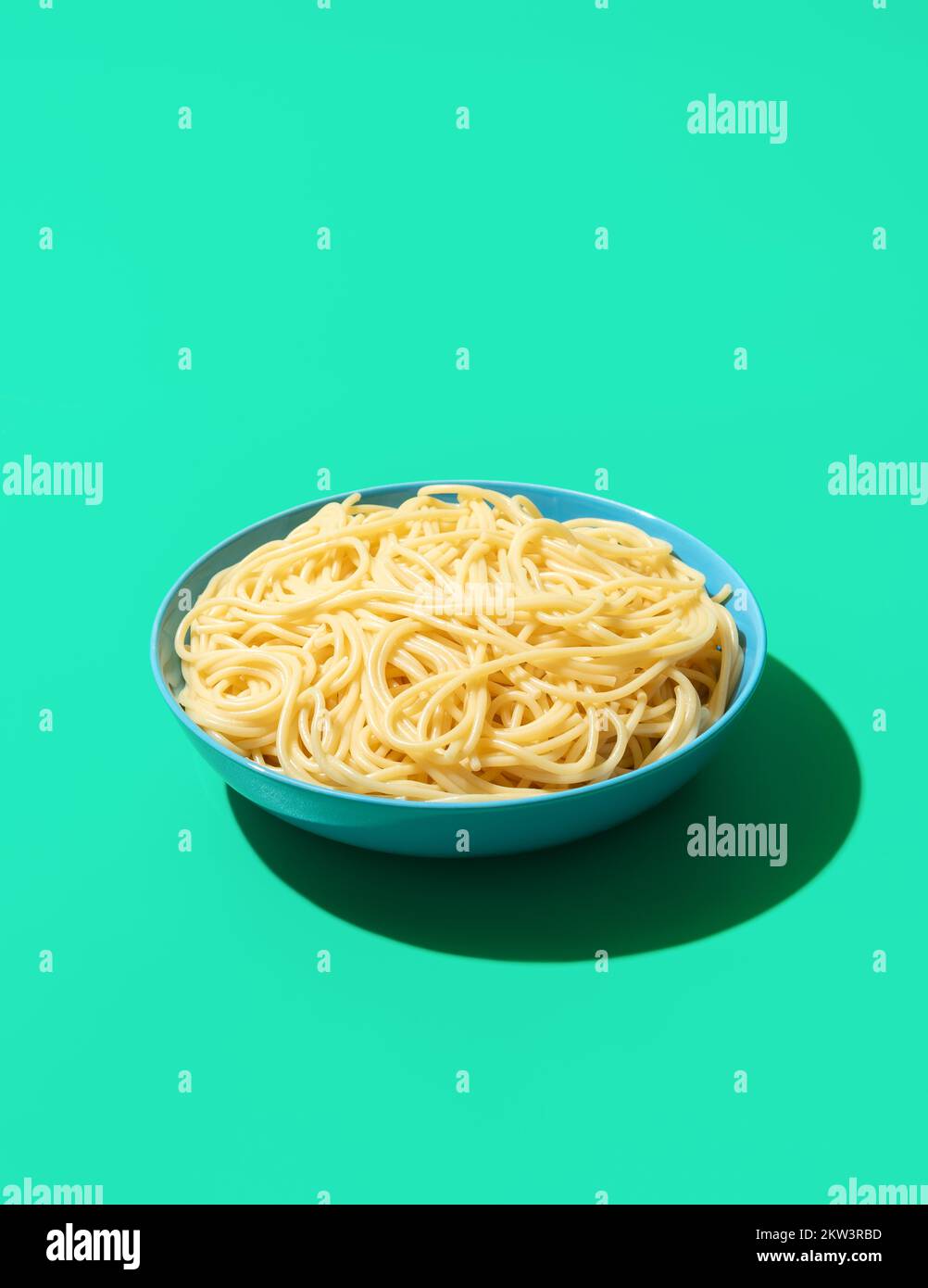Single bowl with cooked spaghetti minimalist on a green table. Pasta without any sauce in a blue bowl in bright light on a colored background Stock Photo