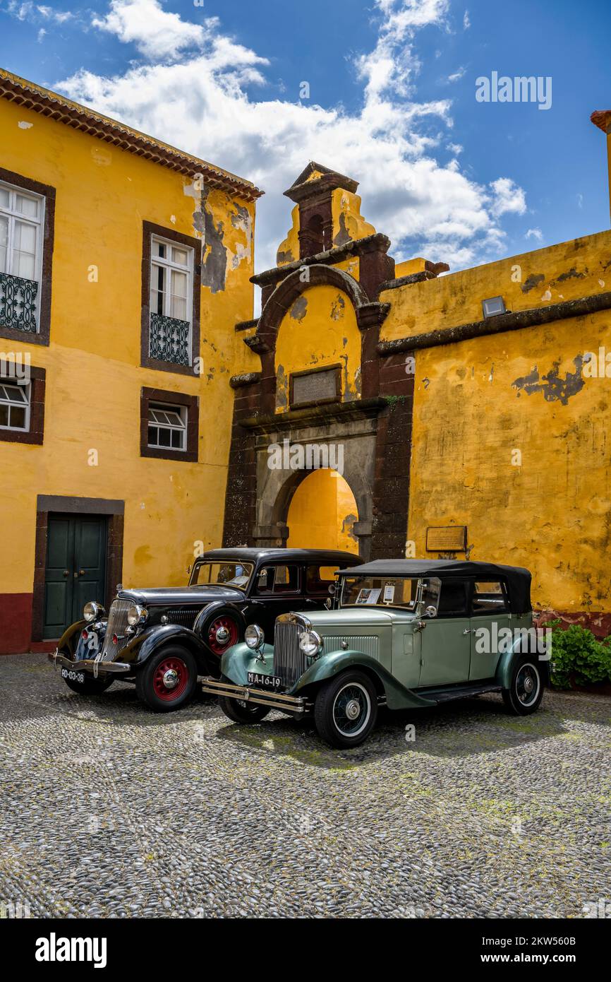 Vintage cars parked in front of yellow gate and wall, Forte de Sao