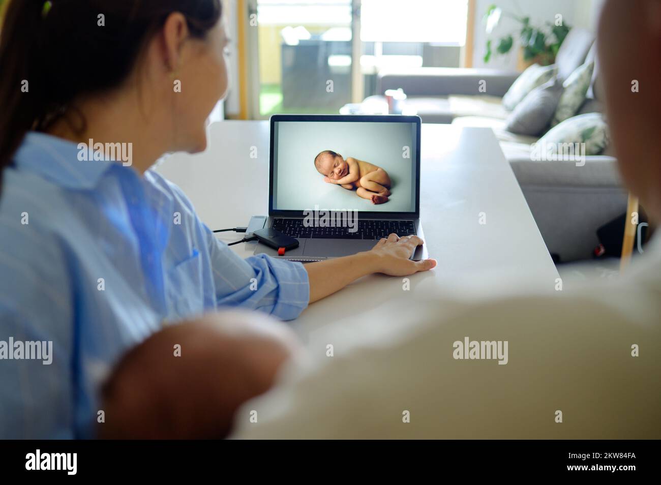 Crop family watching photos of newborn on computer with memory drive Stock Photo