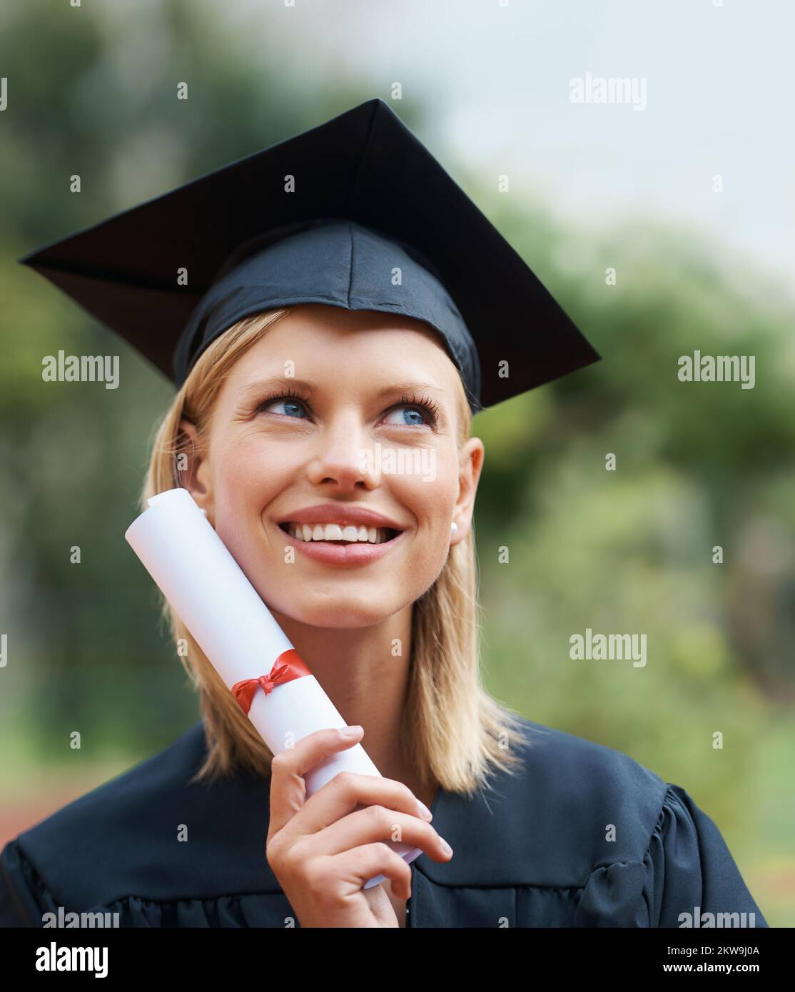Success puts a smile on her face. A young college graduate wearing cap and gown while looking away and smiling. Stock Photo