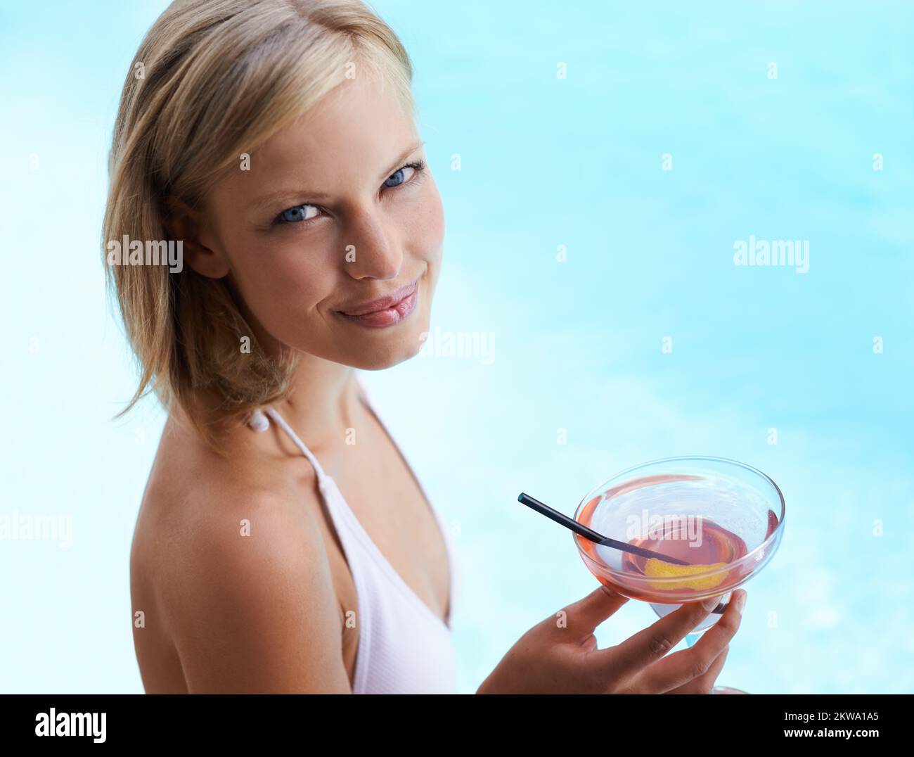 It doesnt get any better than this. a young woman drinking a cocktail by a swimming pool. Stock Photo