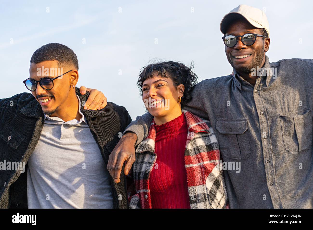 Cheerful multiethnic young friends having fun together and walking embracing together - multiracial woman and African descent young men hugging agains Stock Photo