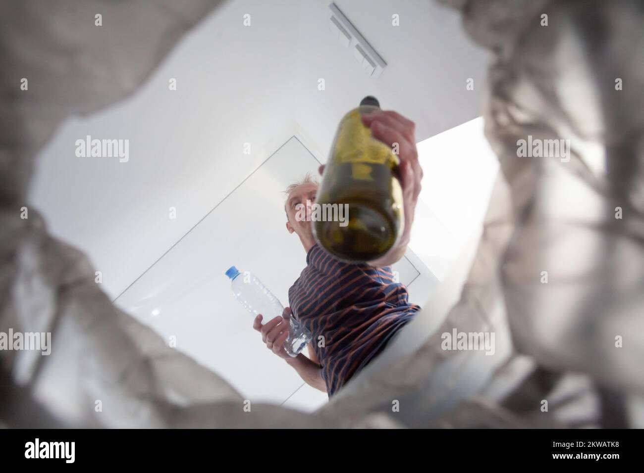 Closeup empty glass bottle in male hand, recycling bin and