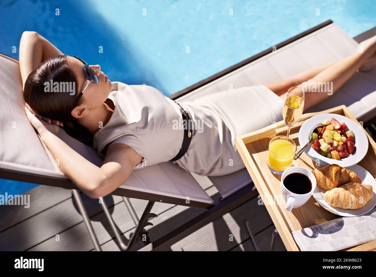 She makes sure to take a vacation every year. An attractive young woman enjoying her poolside breakfast. Stock Photo