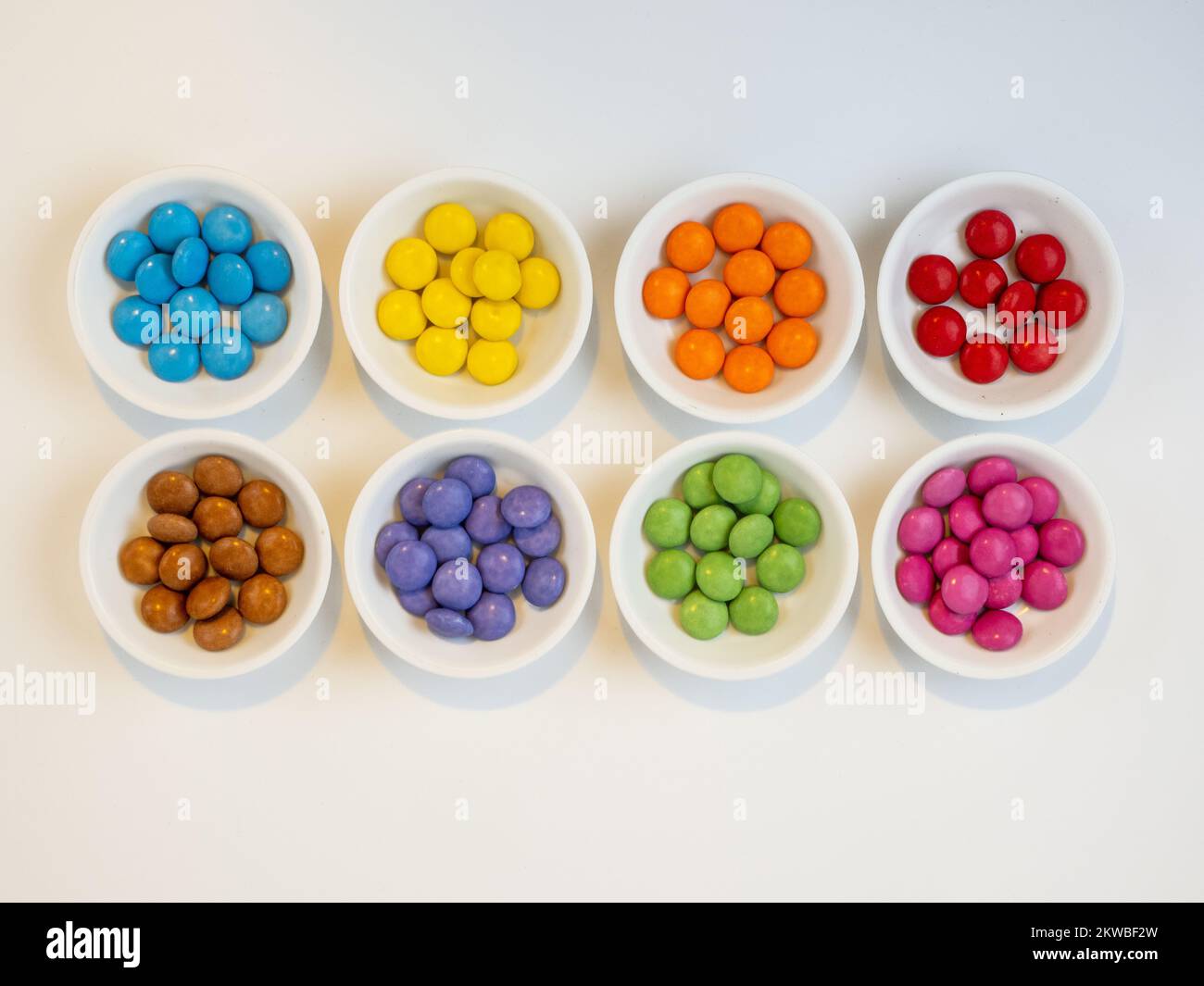 eight bowls of individually colored candy on a white background Stock