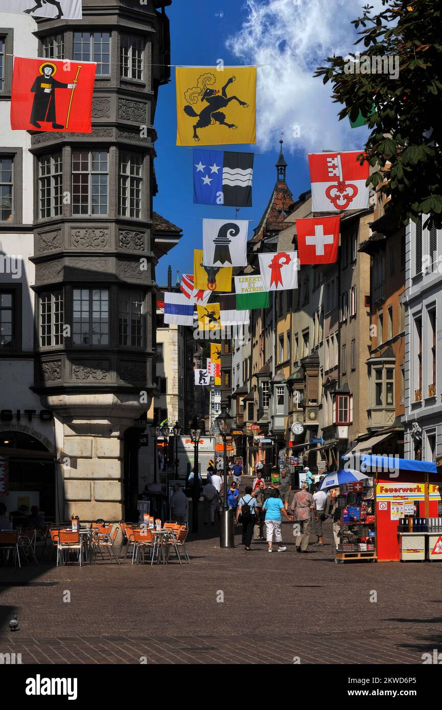 Flags or banners strung across the busy Vordergasse in the old town at Schaffhausen, northern Switzerland, represent the 26 cantons or member states of the Swiss Confederation.  The two nearest the camera are the emblems of Glarus (pilgrim holding a staff and bible) and Schaffhausen (a black ram). Stock Photo
