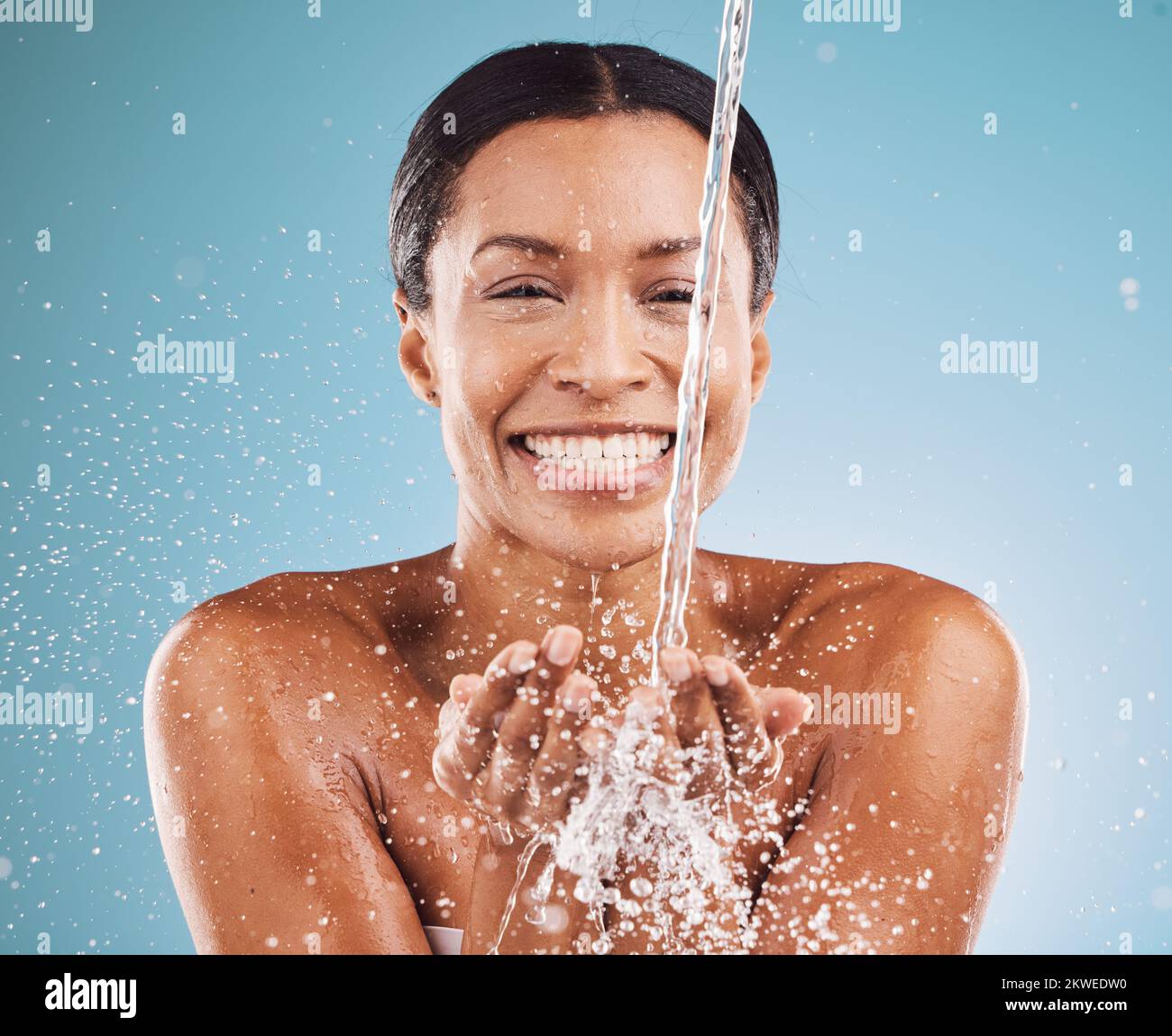 Cleaning, water and black woman with skincare health, beauty wellness and happy shower against blue background in studio. Water splash, cosmetic smile Stock Photo