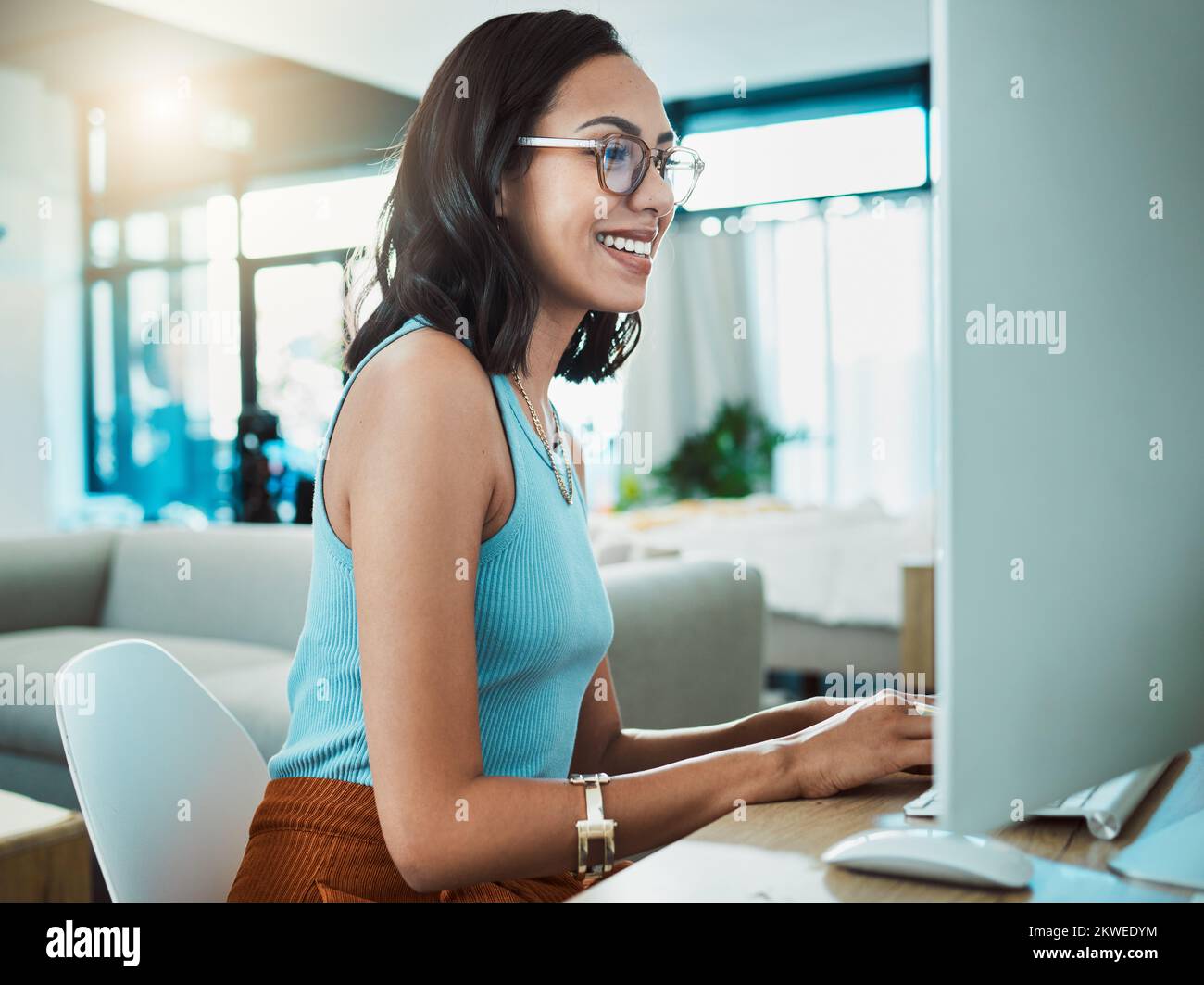 Social media agent with computer browsing online, typing and replying to customer or client emails in home office. Motivated, inspired and smiling Stock Photo
