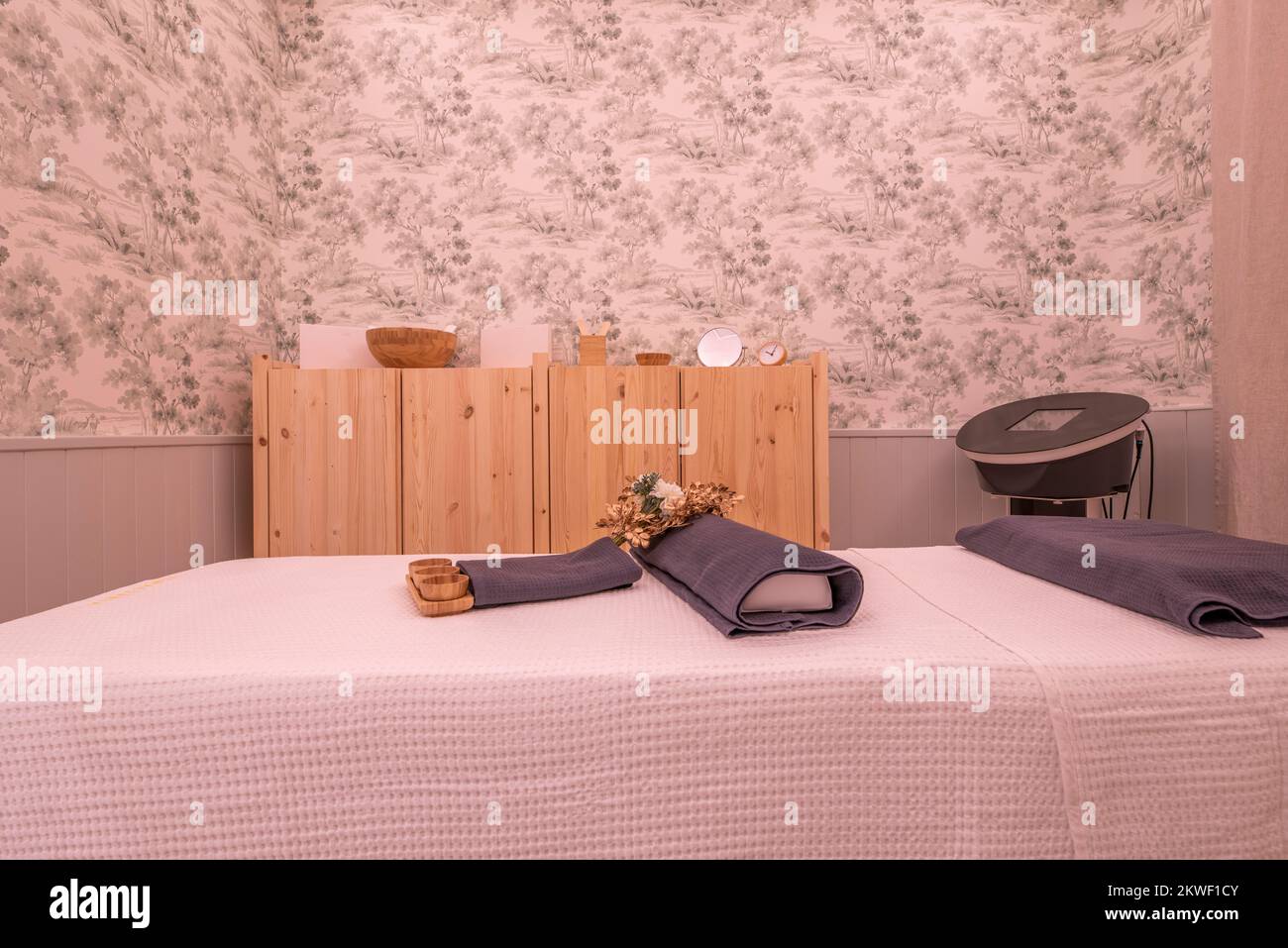 Corner of a cabin for treatments with a table with objects for massage with wood in a beauty and relaxation salon and walls with decorative wallpaper Stock Photo