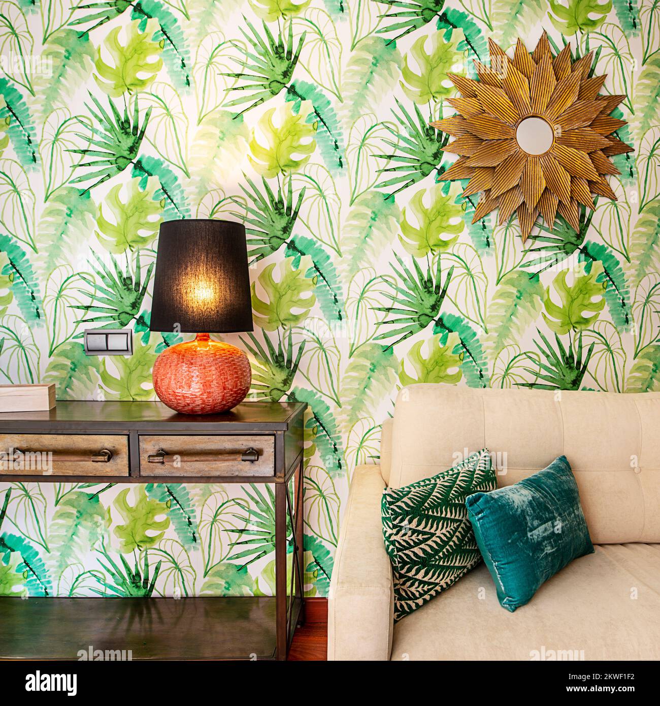 Detail of a living room with a sofa upholstered in beige fabric with green cushions, an industrial style sideboard and wallpapered wall and gold desig Stock Photo