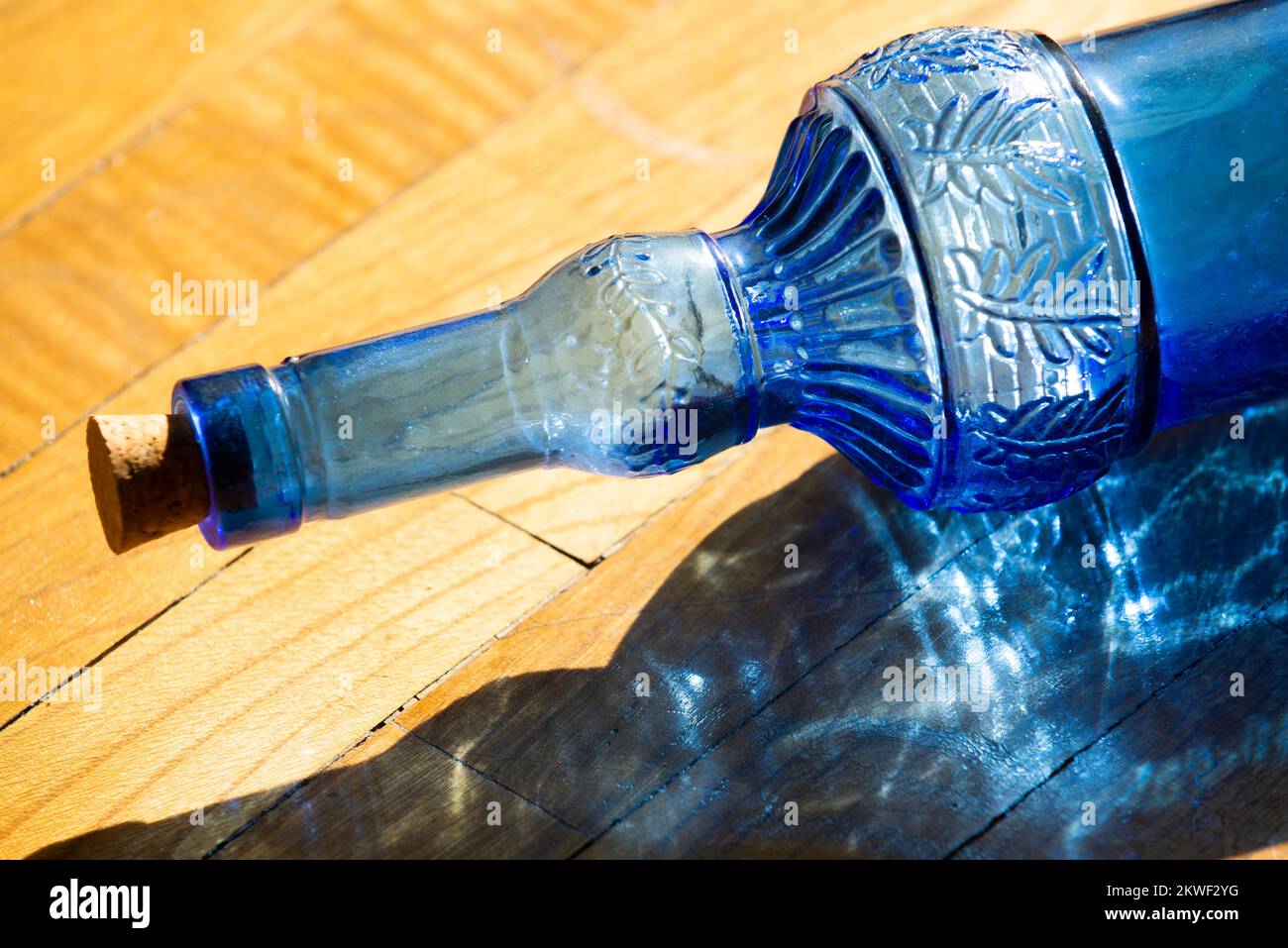 A blue decorative glass bottle on an oak surface pierced by a large ray of morning sun Stock
