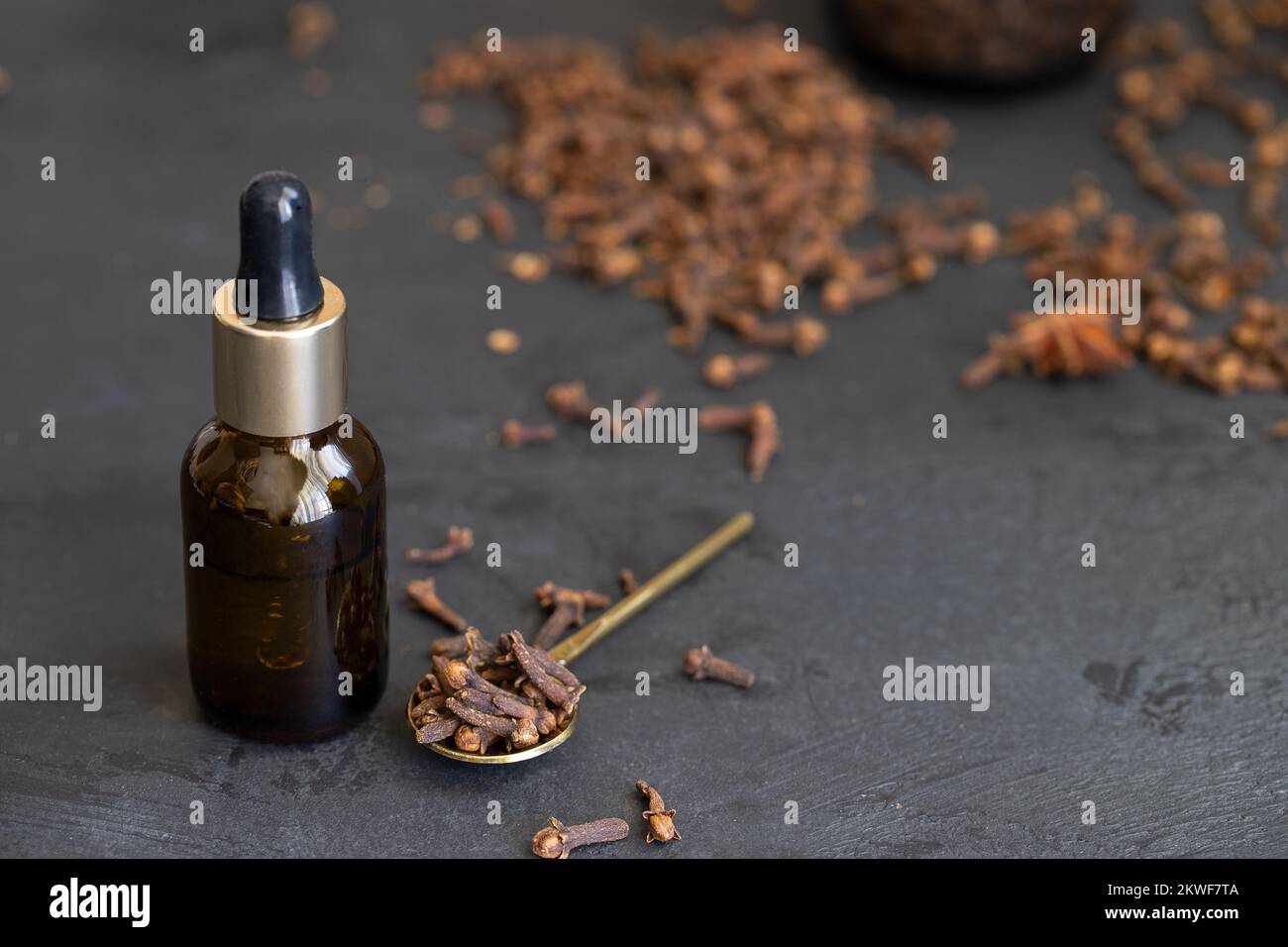 Essential clove oil in glass bottle and natural clove spice on a dark