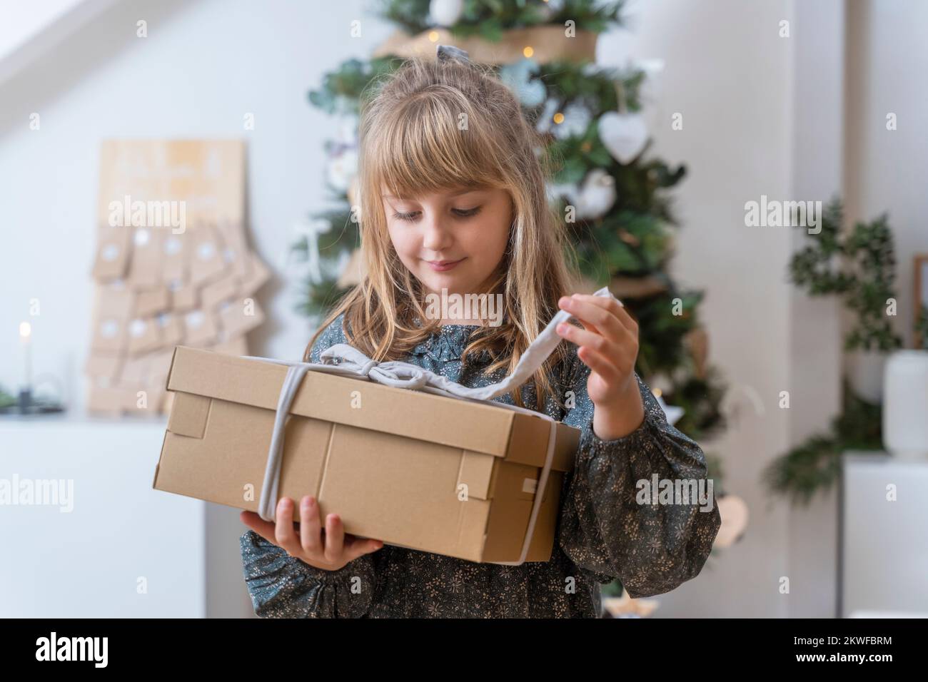 Little girl opening a gift near the christmas tree at home Stock Photo