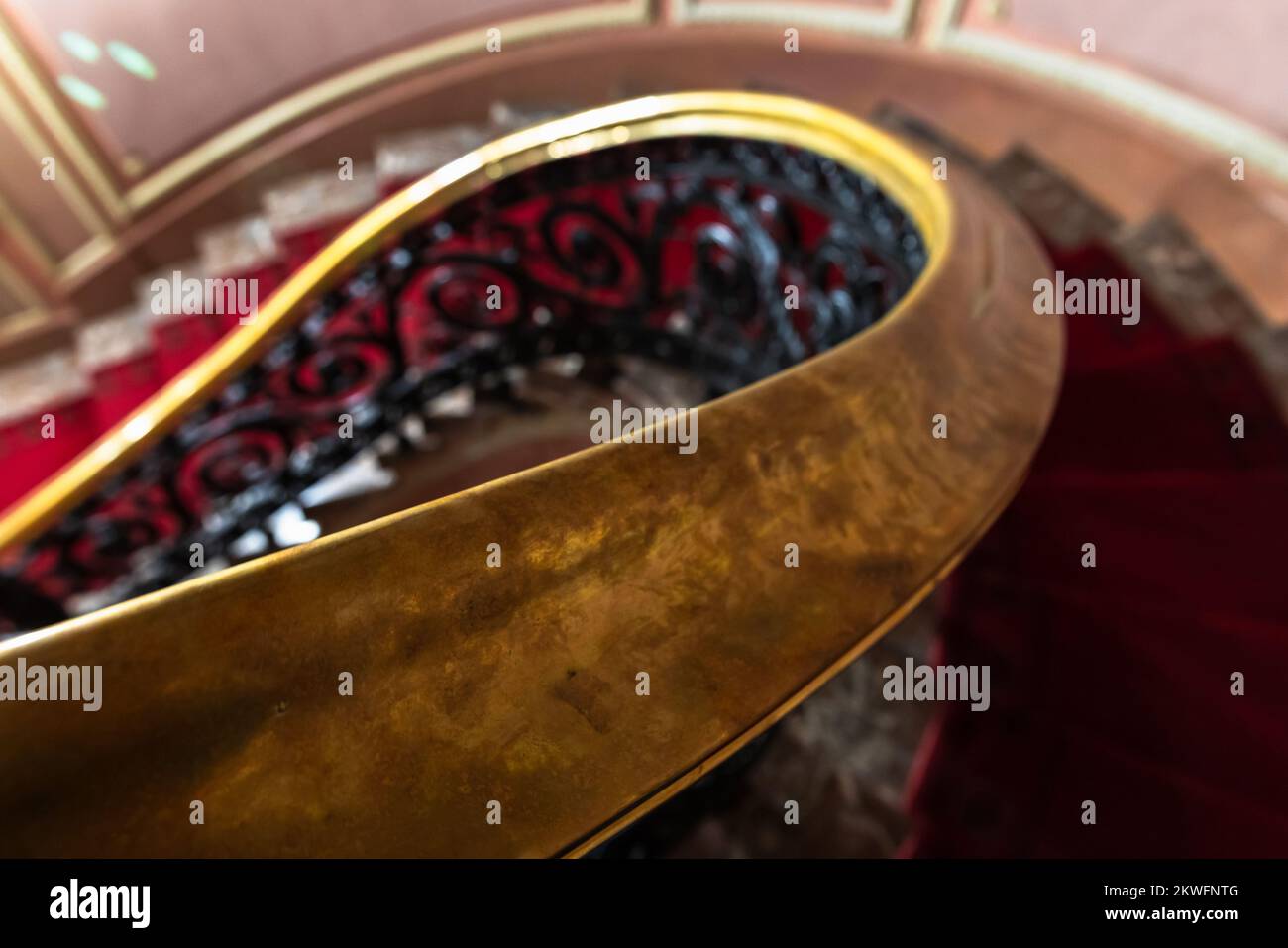 Brass handrail of a spiral staircase with red carpet. Vintage classic