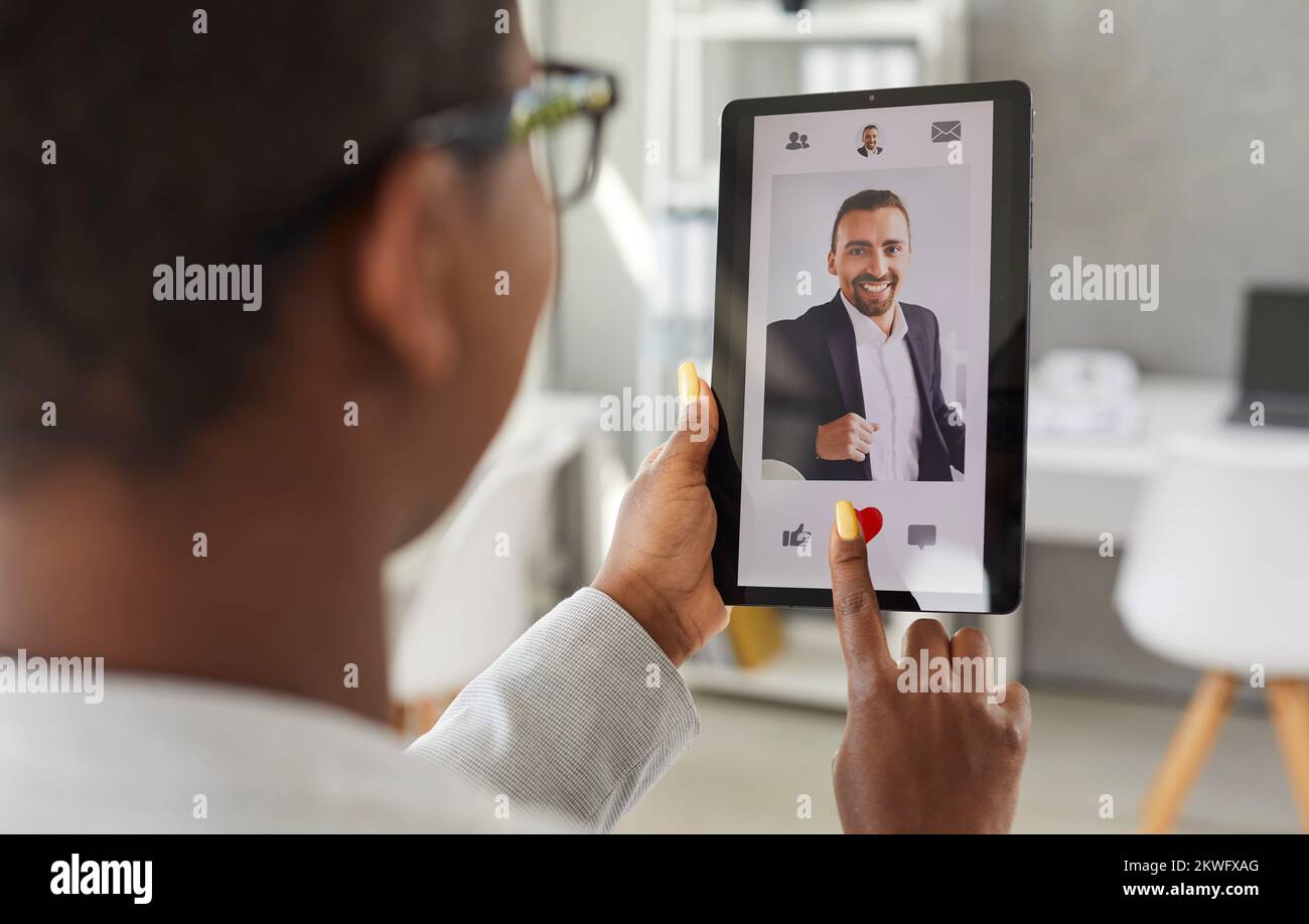 Woman uses tablet and gives like to photo of man on online dating app or website Stock Photo
