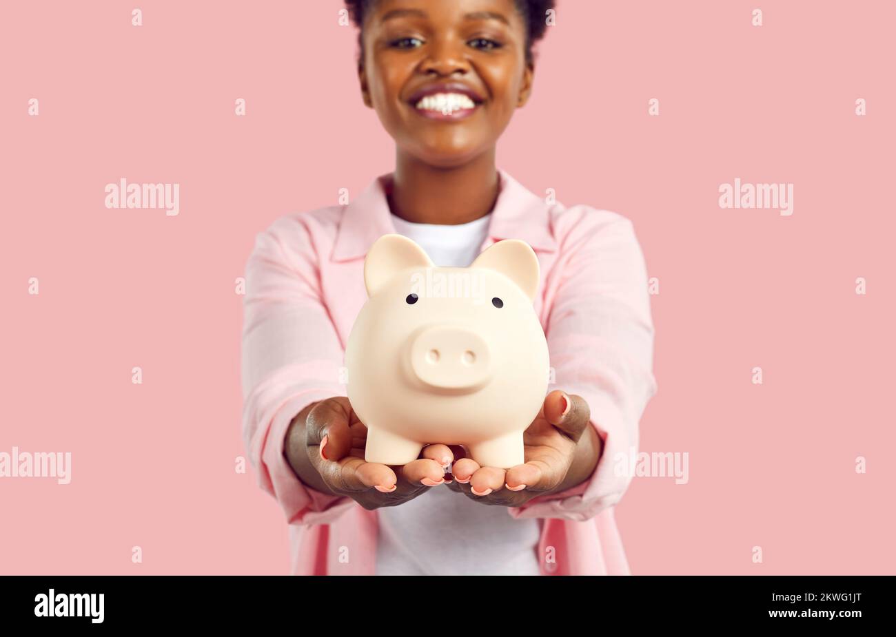 Portrait of happy smiling african american woman holding piggy bank in hands on pink background. Stock Photo