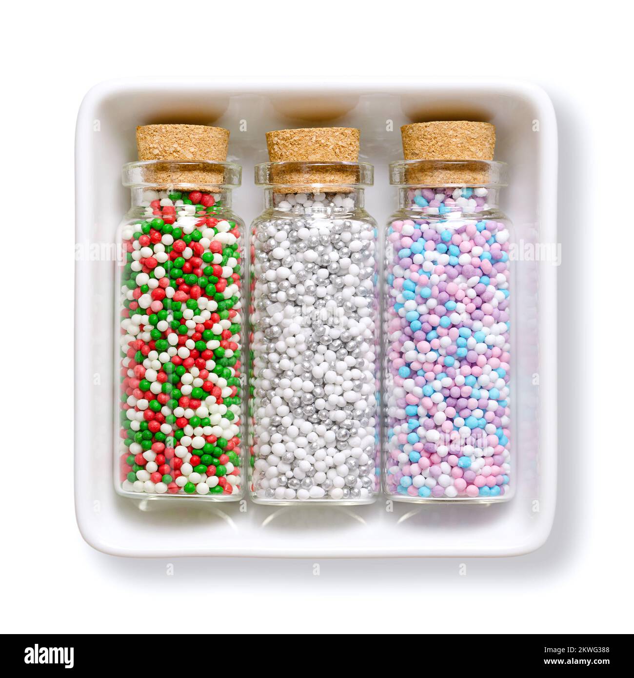 Nonpareils, in glass bottles, in white bowl. Winter and christmas colored mixes of edible confectionery of tiny sugar balls. Hundreds and Thousands. Stock Photo