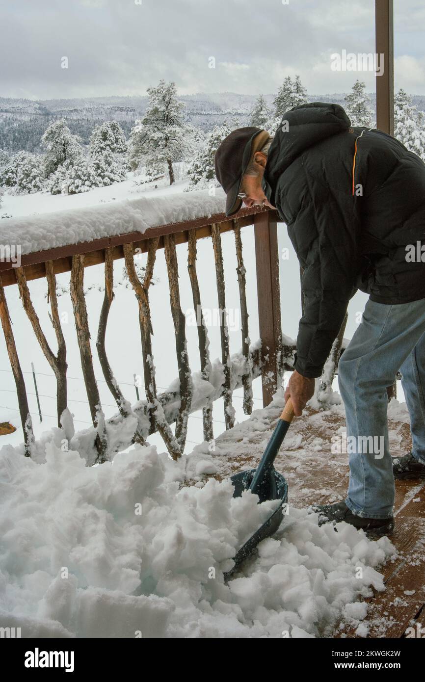 Senior male shovels snow off of a wooden deck. Stock Photo