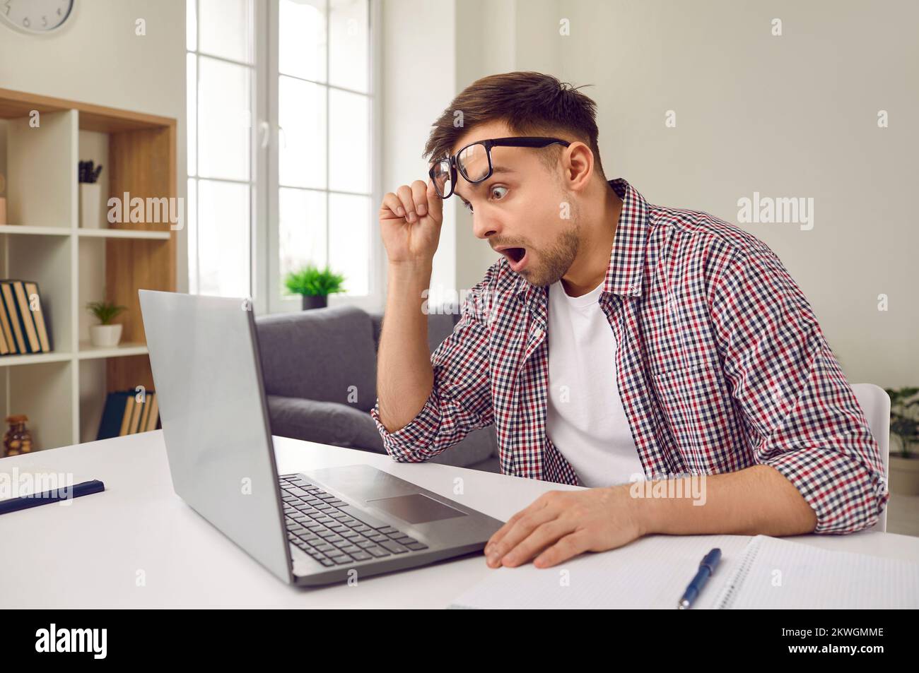 Man is looking at laptop screen with shocked, confused and scared expression on his face. Stock Photo