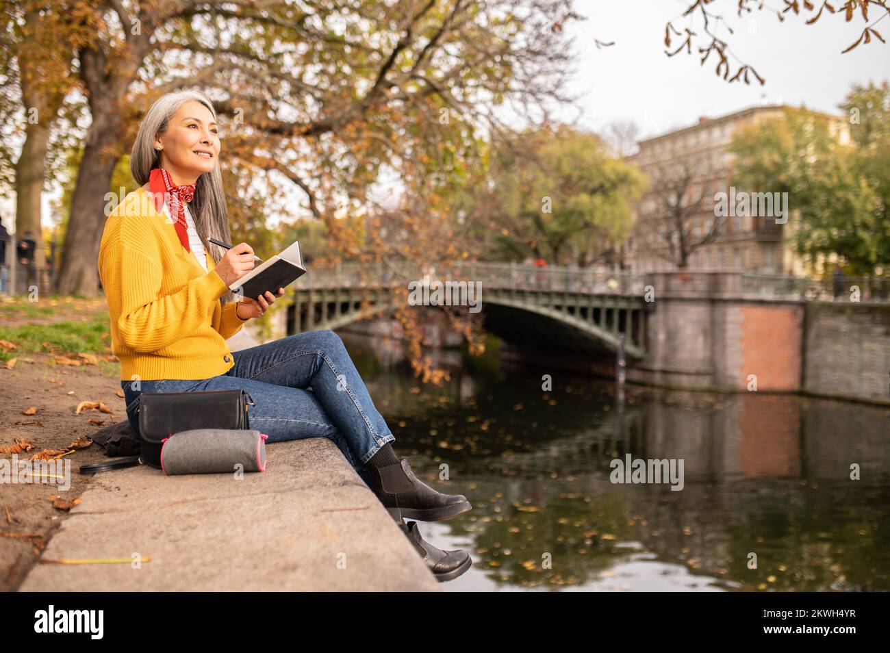 Woman sitting on the river bank, making notes and looking inspired Stock Photo