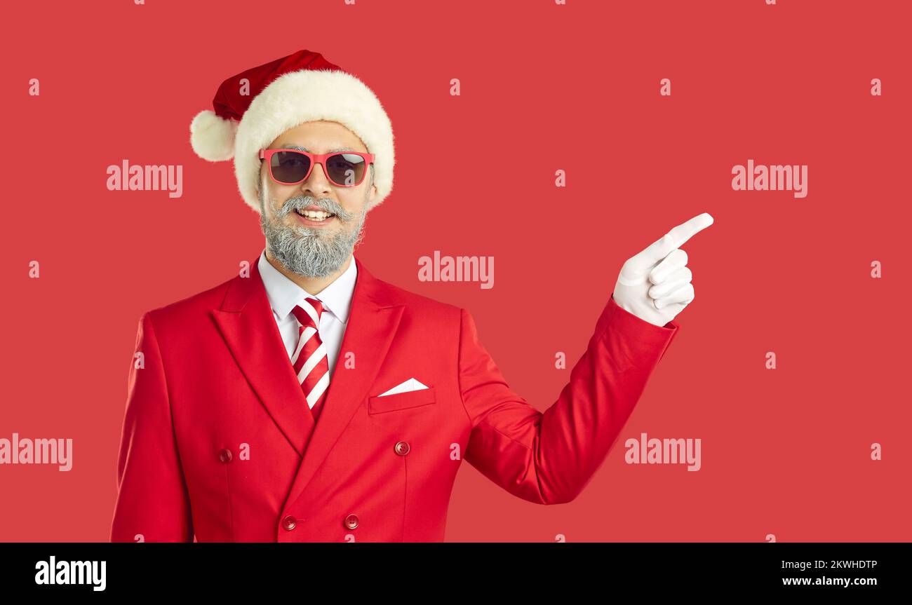 Man in Christmas costume standing on red color background and pointing finger to side Stock Photo