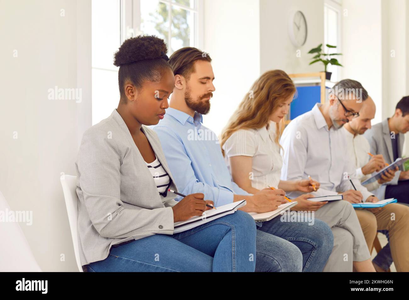 Diverse audience taking notes while listening to lecture at business conference Stock Photo