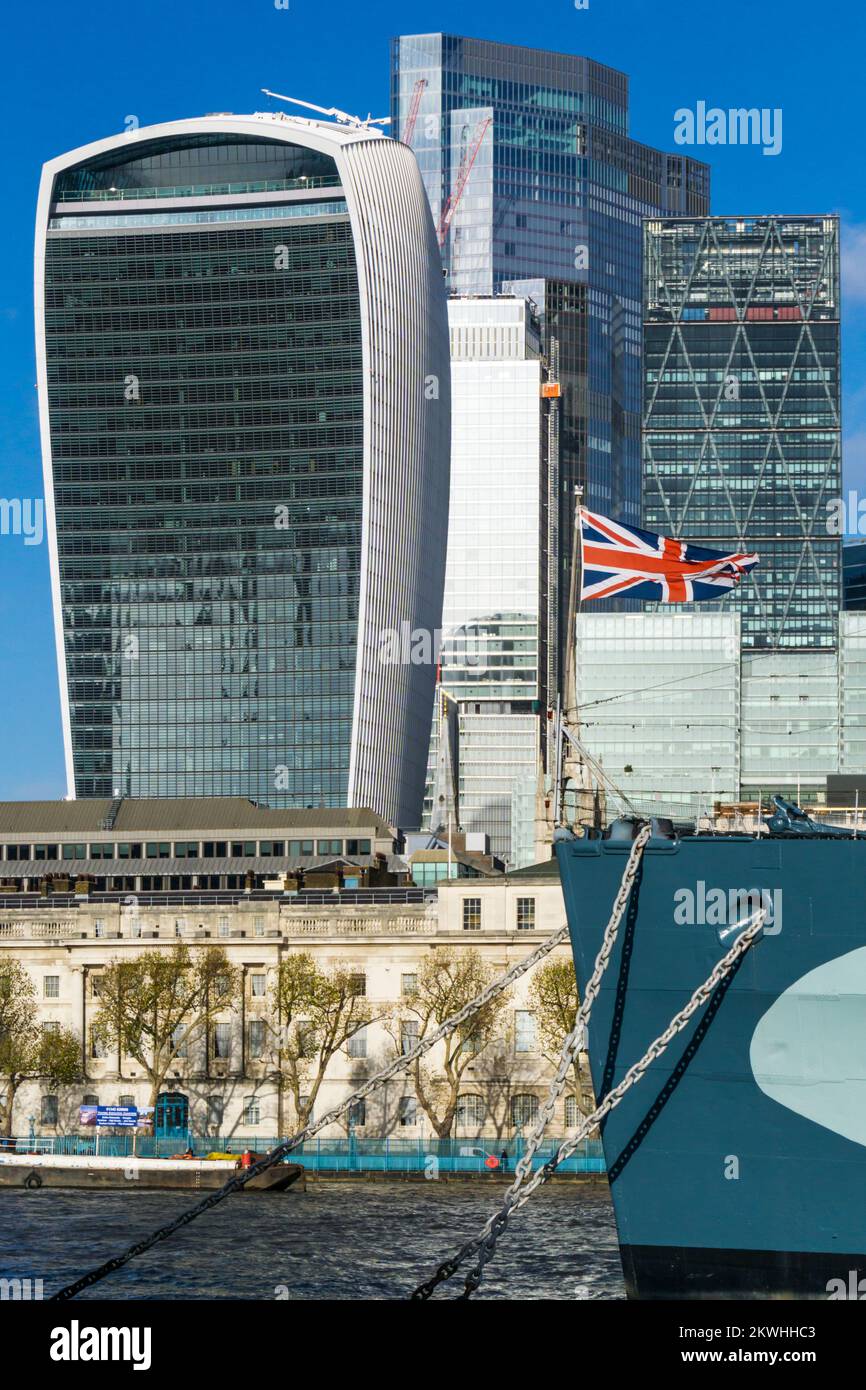 Union Jack flag on bow of HMS Belfast in front of the office blocks of the City of London. Stock Photo