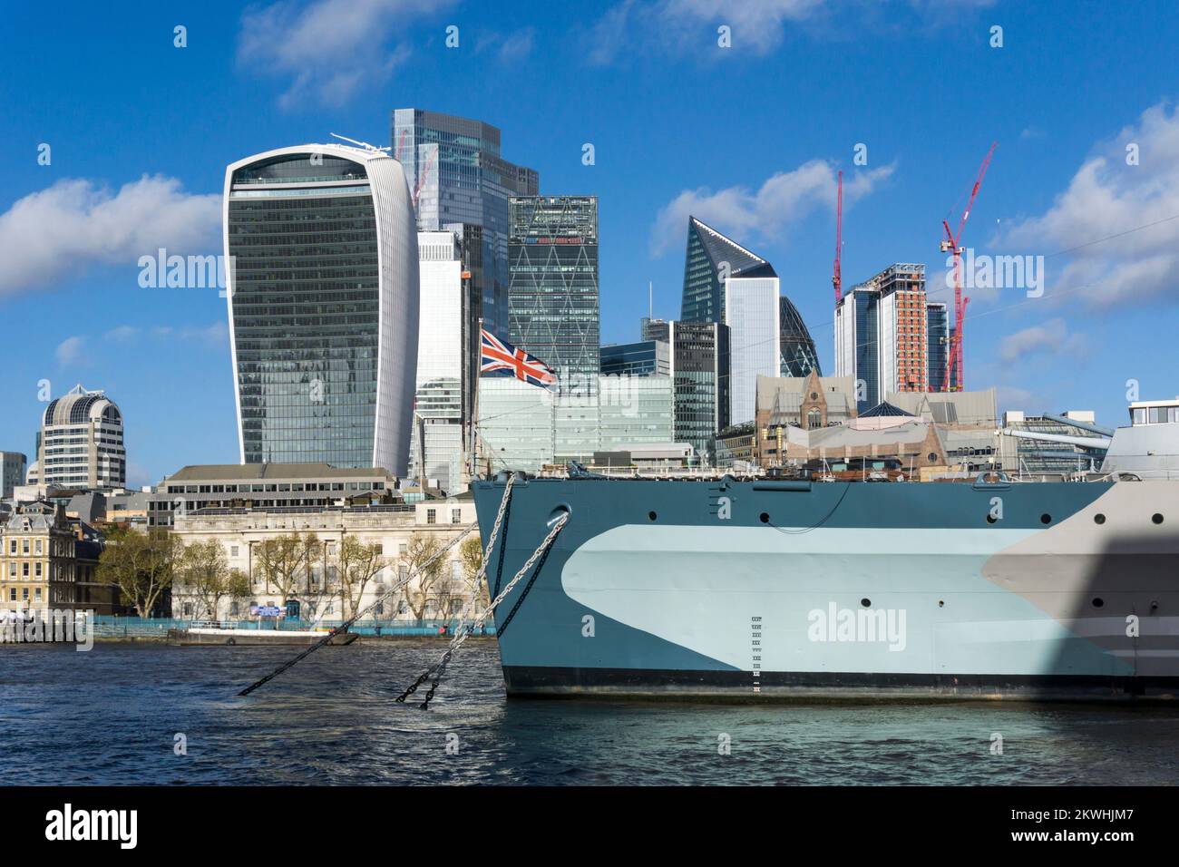 Union Jack flag on bow of HMS Belfast in front of the office blocks of the City of London. Stock Photo