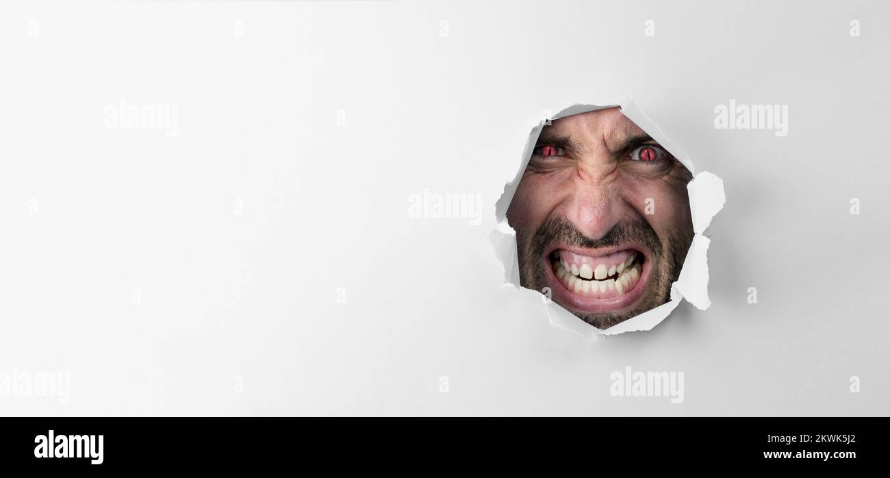 Angry insane man looking through the hole with red eyes on white background with copy space for advertising Stock Photo