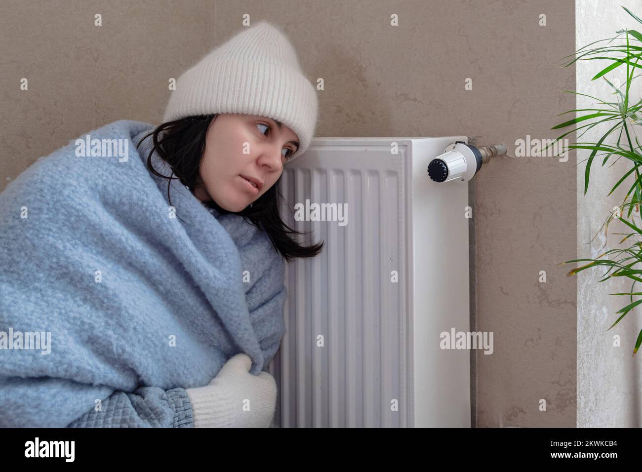 sad woman tries to warm herself by the radiator Stock Photo