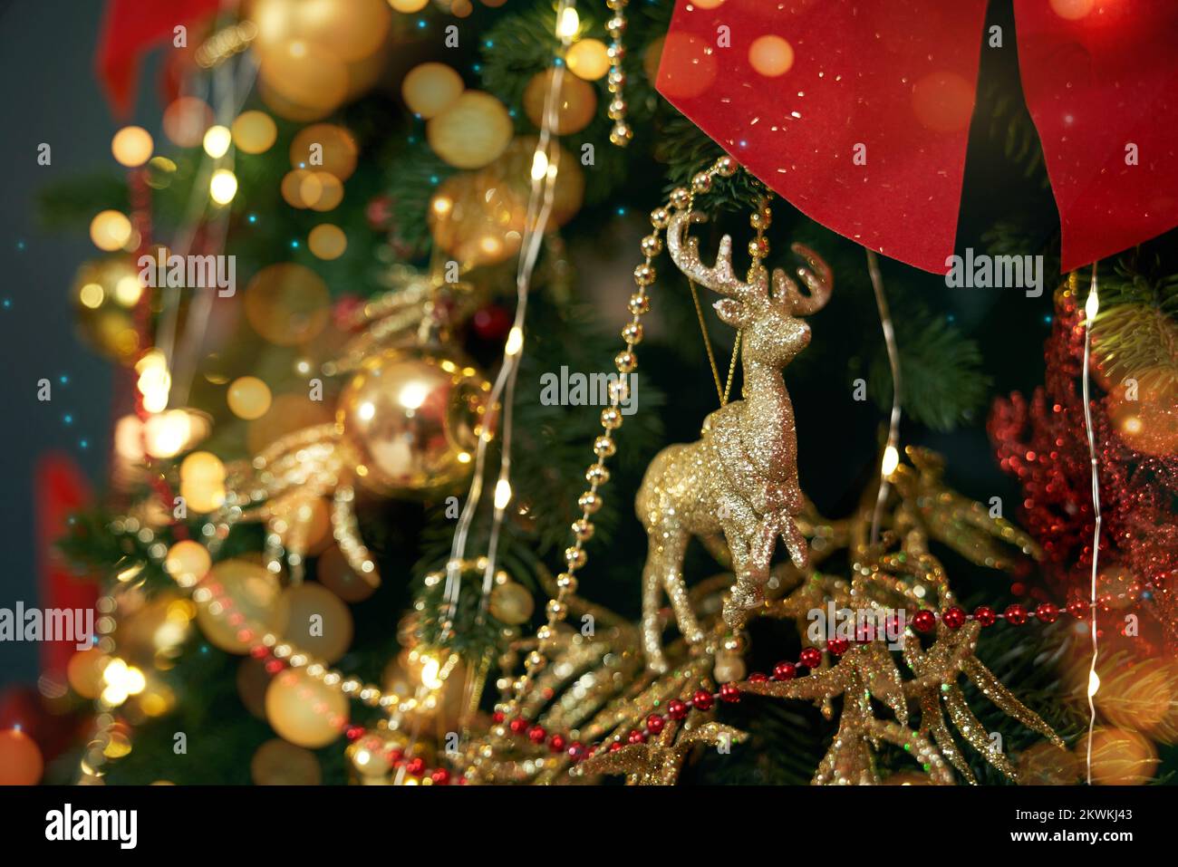 Close up of Christmas tree standing, decorated with golden deer, sparkling. People celebrating New Year in decorated room, expecting. Concept of New Year and celebration. Stock Photo