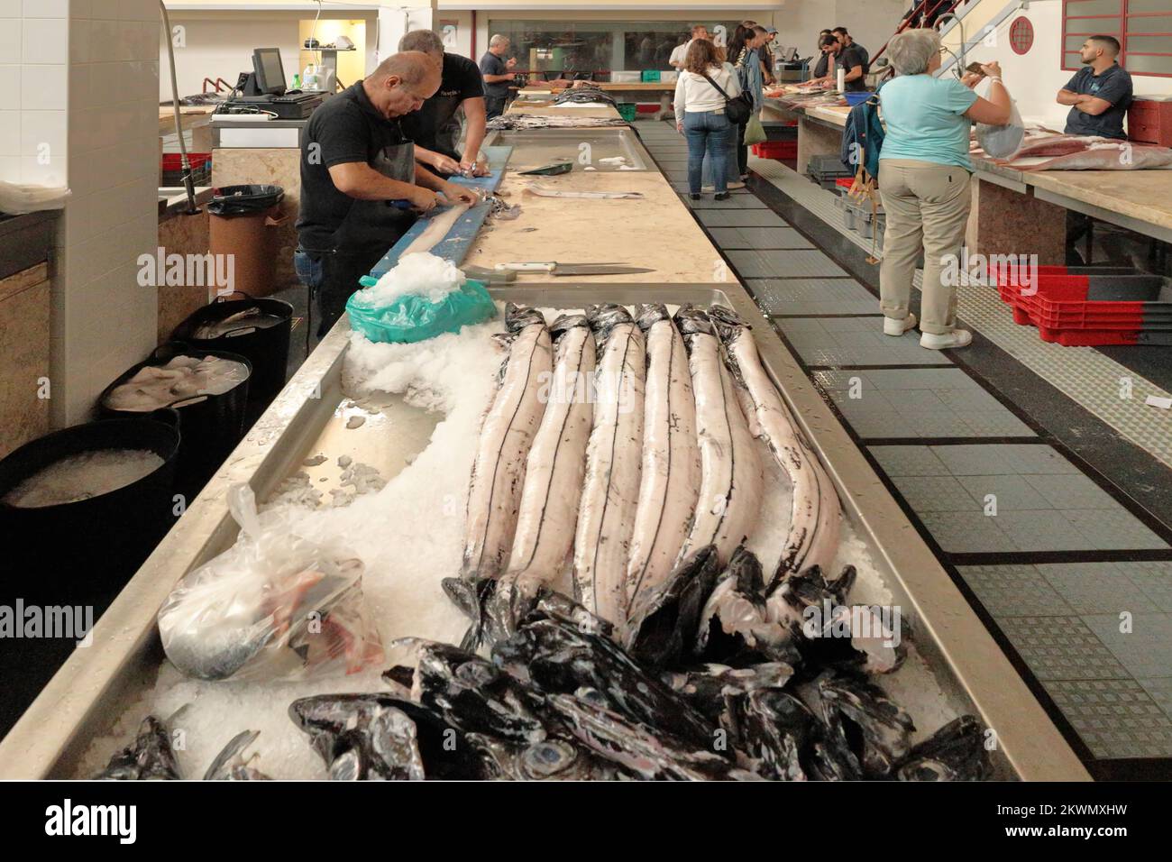 Funchal fish market, Madeira - fishmongers preparing Black Scabbard Fish or Espada while shoppers browse the fish on sale Stock Photo