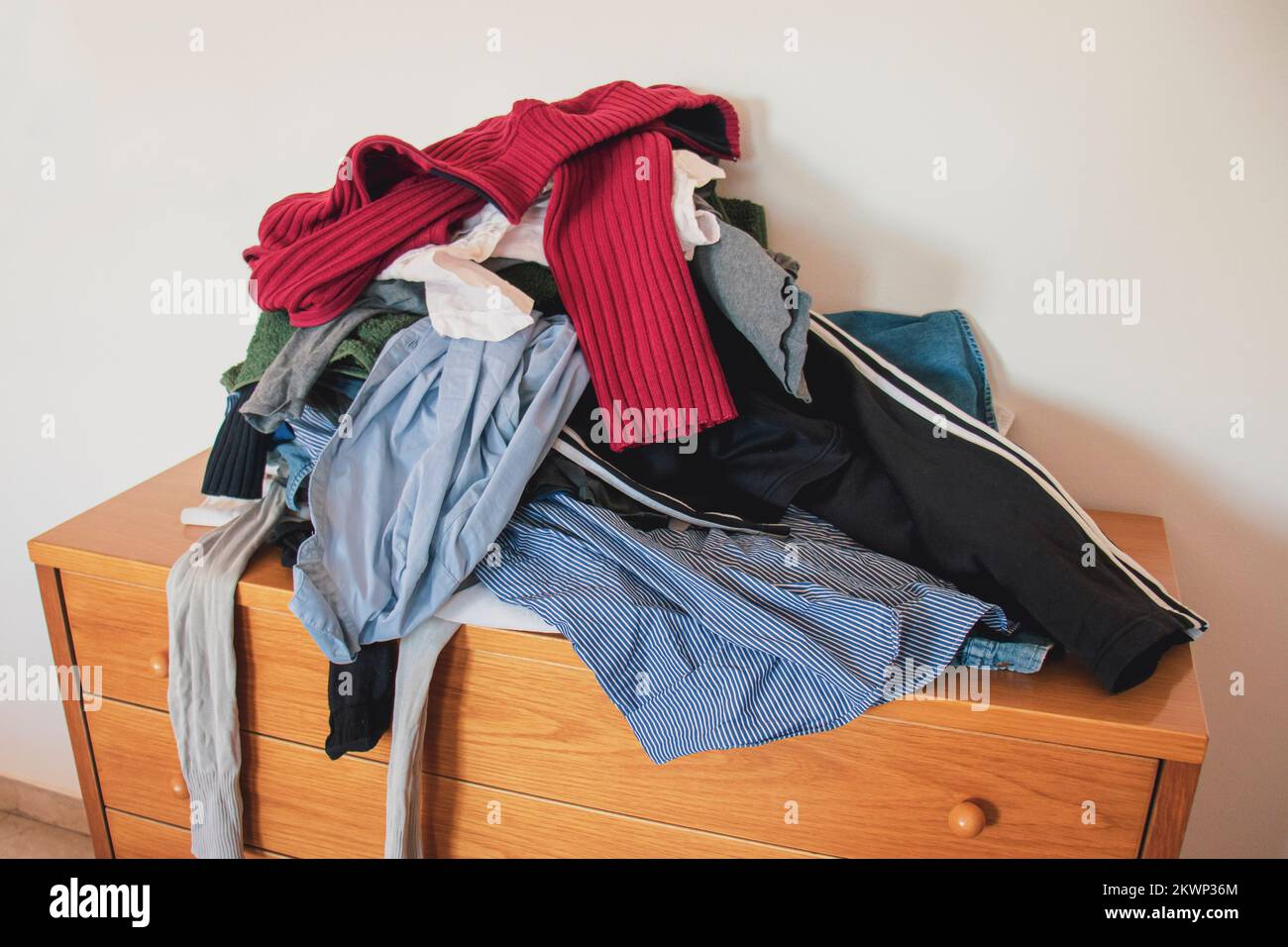 Pile of unfolded clothes on a for laundry on a drawer. Concept of minimalism, mess and wardrobe cleaning. Stock Photo