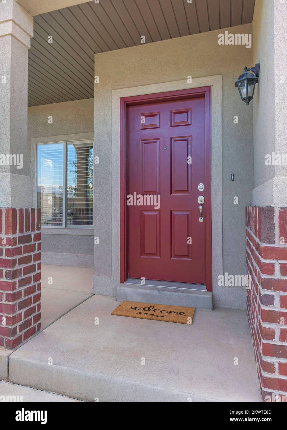 Vertical Red front door of a house with red bricks siding and railings at the porch. Front porch of a house with a view of the neighbor's house garage Stock Photo