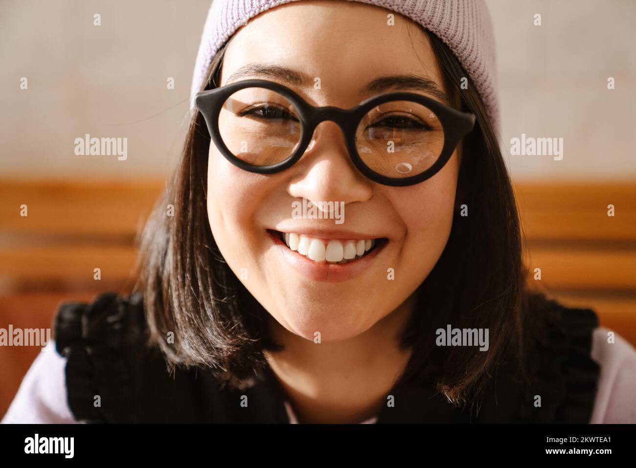 Young asian woman in eyeglasses smiling and looking at camera indoors Stock Photo