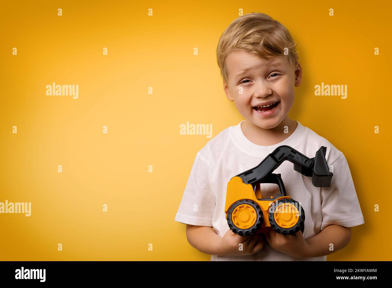 little smiling boy with toy tractor in hands on yellow background with copy space Stock Photo