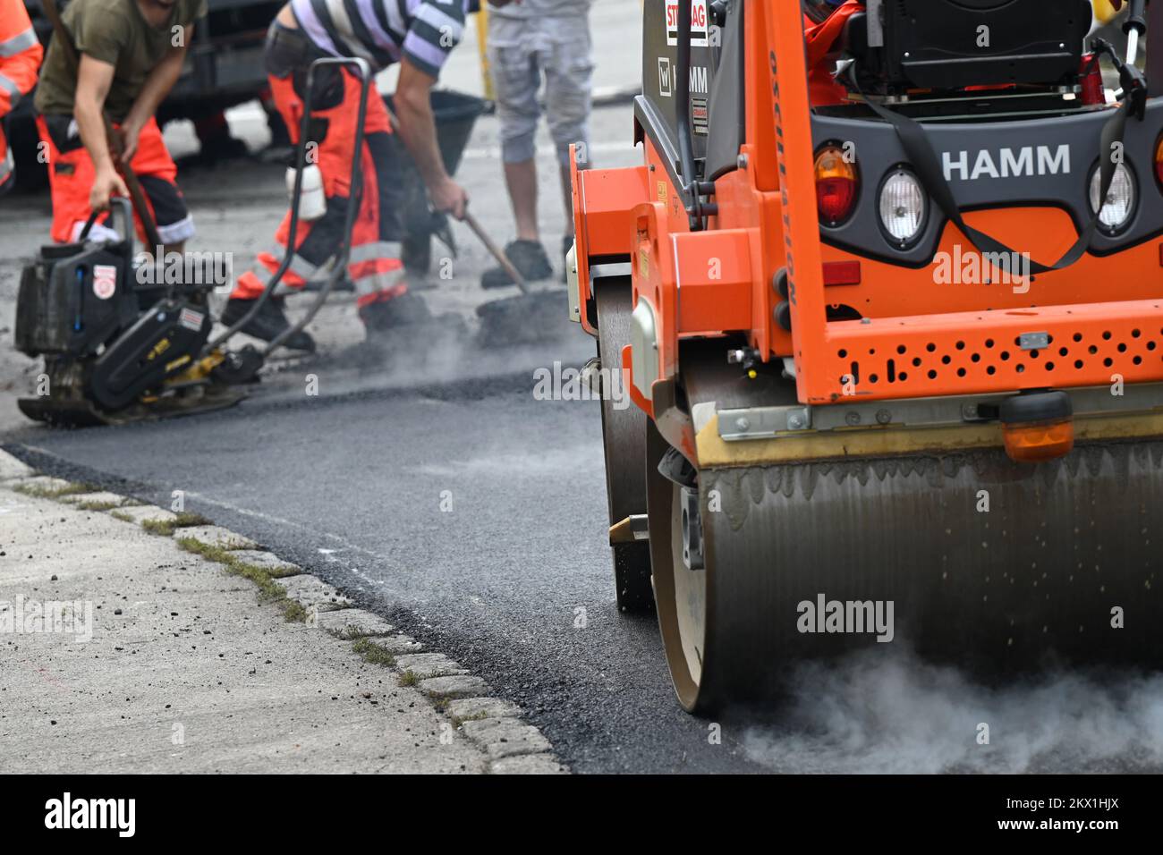 A road roller paving, in the background the feet of workers Stock Photo