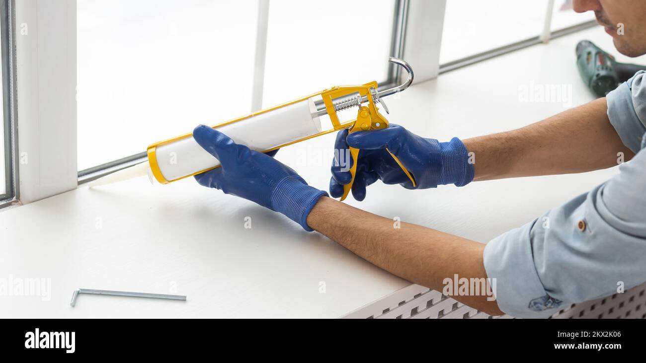 Construction worker sealing window with caulk indoors Stock Photo