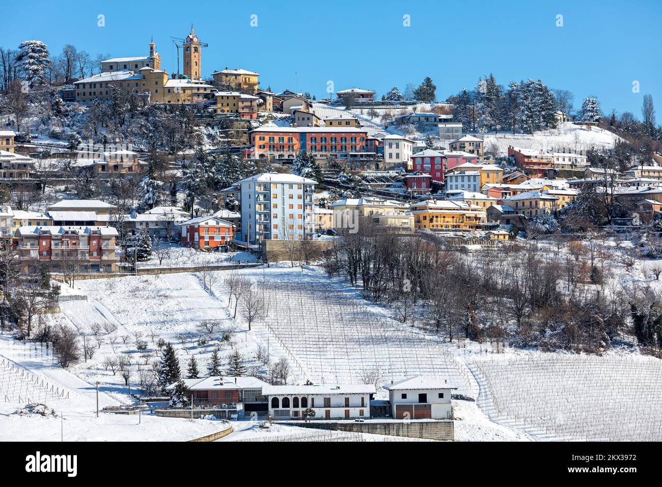 View of small town on snowy hill under blue sky in Piedmont, Northern Italy. Stock Photo