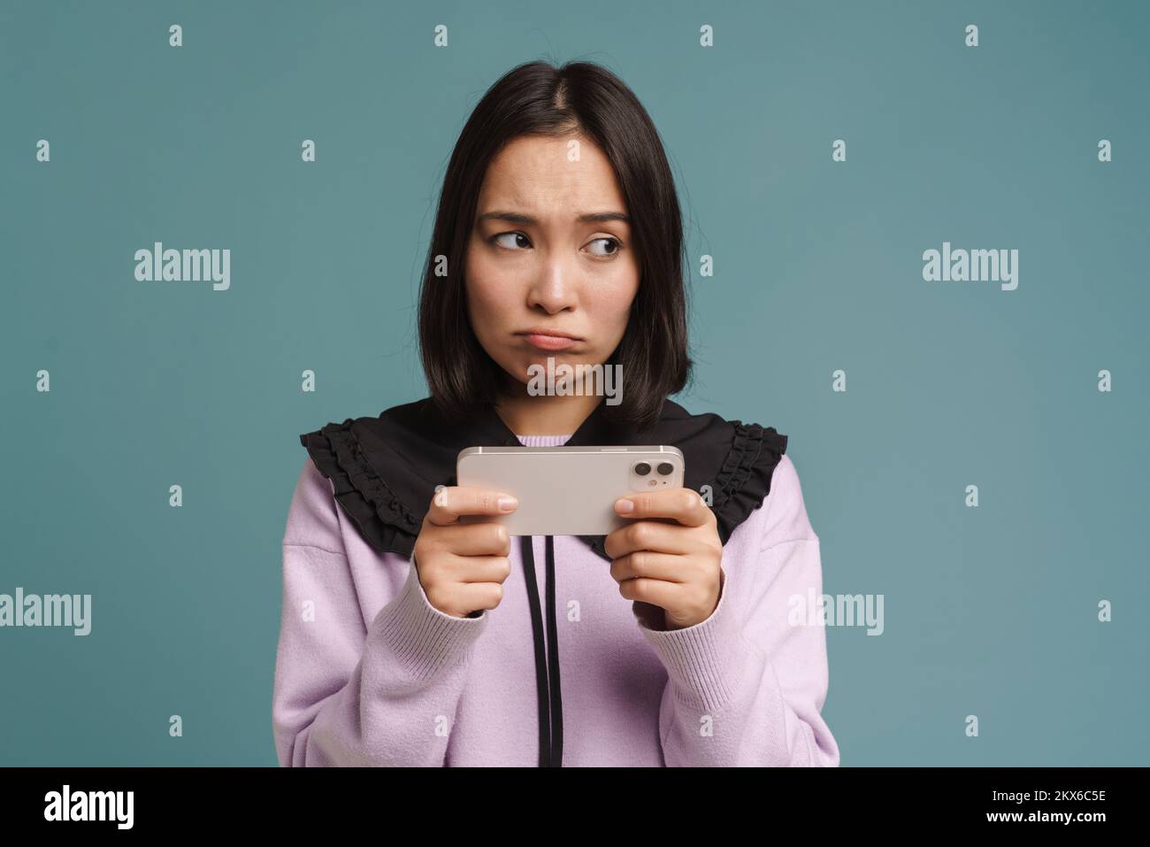 Young asian woman playing online game on mobile phone isolated over blue background Stock Photo